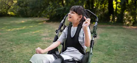Smiling girl seated in a supportive mobility chair outdoors on a lawn after Cerebral Palsy