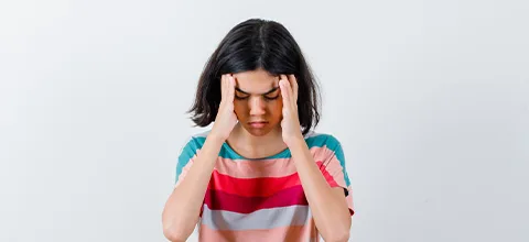 Girl with eyes closed pressing her fingertips to her temples because of a headache