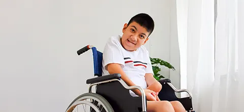 smiling boy with neuromuscular disorders on a wheelchair beside a sunlit window 